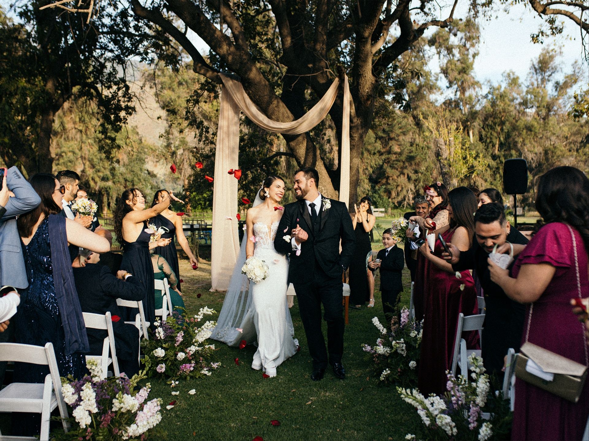 Alegre salida de recién casados tras ceremonia de matrimonio al aire libre en jardín de Chile. Captura documental de momentos auténticos y emotivos por Bodafilms.cl.